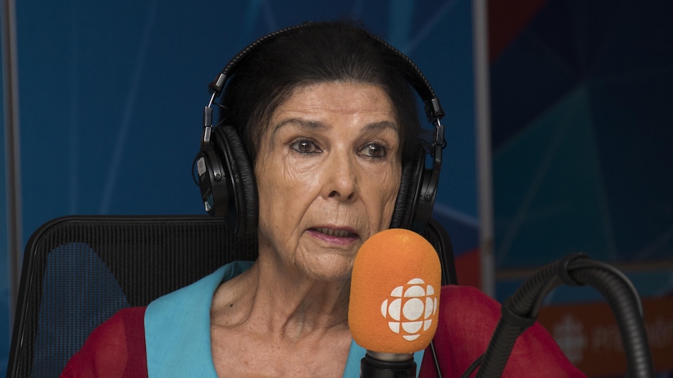 Alanis Obomsawin dans le studio 17 de Radio-Canada, assise devant un micro orange.