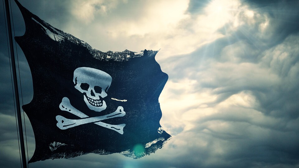 Un drapeau noir orné d’une tête de mort devant un ciel nuageux.