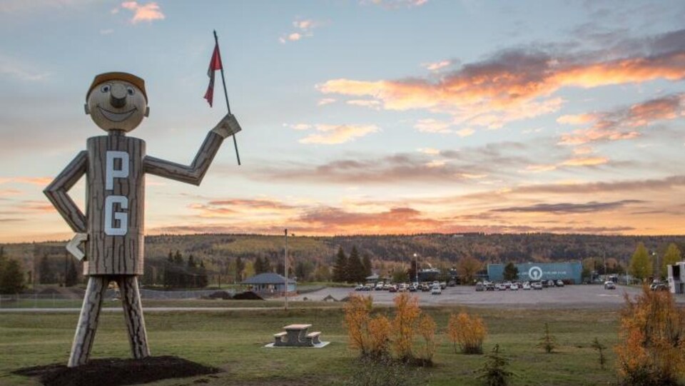 Une gigantesque figurine de bois avec les lettres P et G écrites sur lui tient un drapeau canadien.