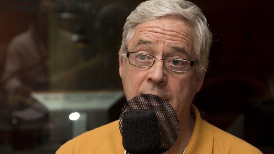 Il parle derrière un micro noir dans un studio radio.