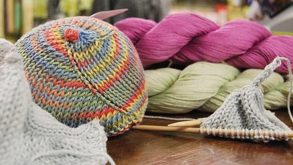 Un sein tricoté, deux épingles à tricoter du fil de coton sur une table.