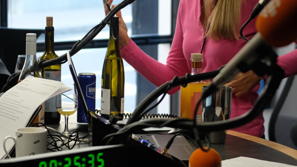 Une femme parle dans un studio radio, des bouteilles d'alcool sont sur la table devant elle.