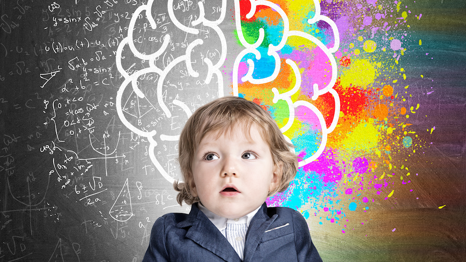 Portrait d'un adorable garçon portant un complet et posant devant un tableau sur lequel se dessinent des formules mathématiques et l'esquisse d'un cerveau en partie coloré en de multiples couleurs. Un concept illustrant l'intelligence et la créativité de l'enfant.