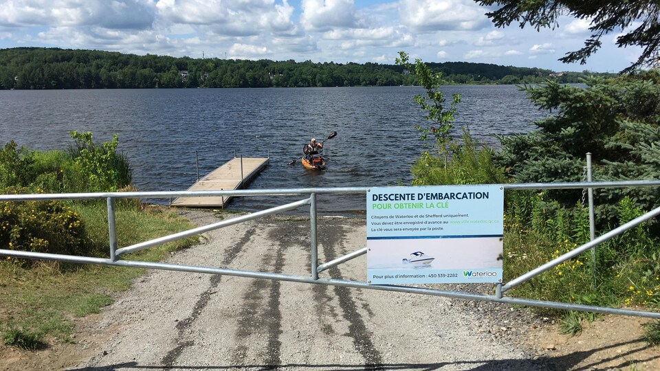 Une barrière barrant l'accès à un lac sur lequel se trouve un kayakiste.