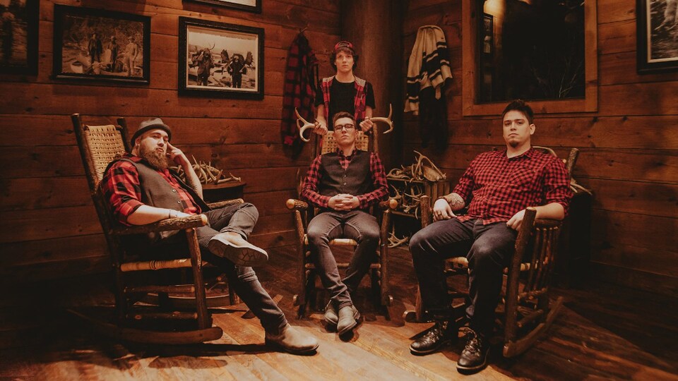 Photo de quatre hommes portant des chemises ou une veste à carreaux dans un chalet en bois traditionnel.