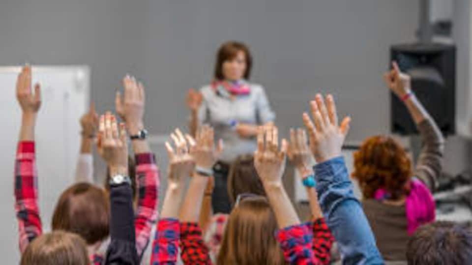 Des élèves lèvent la main dans une salle de classe.  