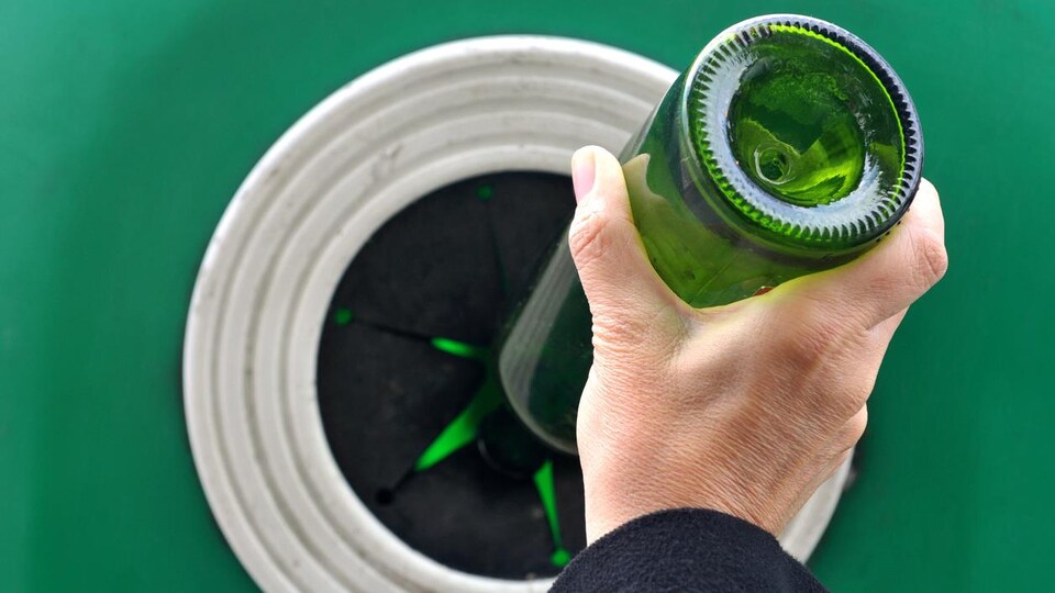 Photo d'une personne mettant une bouteille en verre dans un bac de recyclage.
