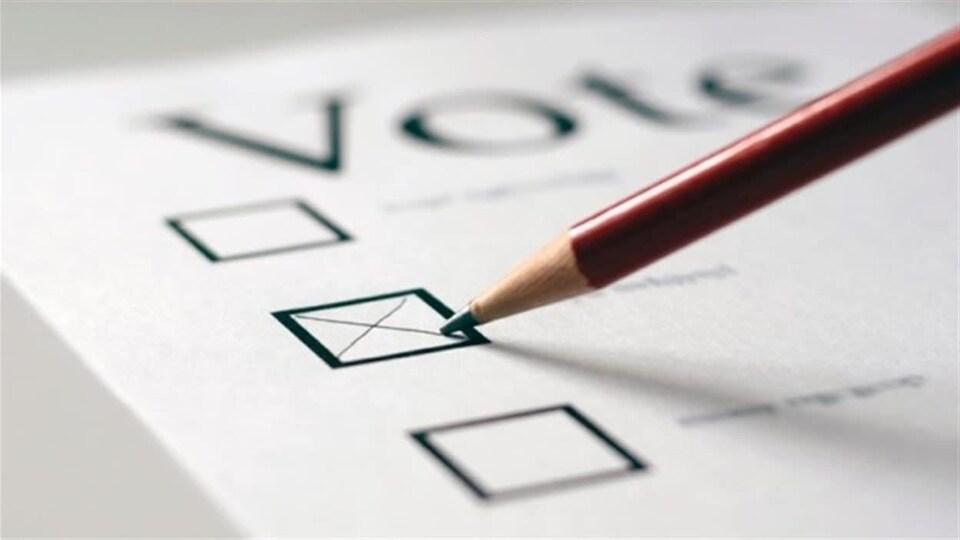 Plan serré d'un crayon de plomb qui trace une croix sur un bulletin de vote.