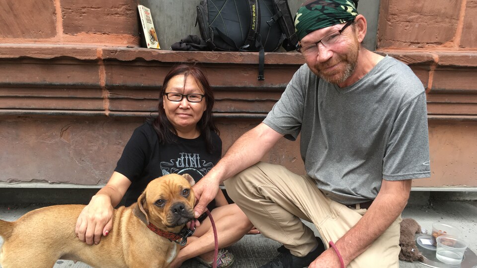 Une femme et un homme assis sur le trottoir en compagnie d'un chien.
