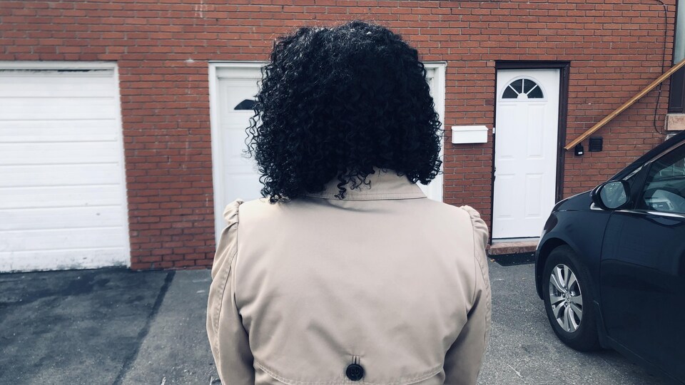 Une femme debout dans le stationnement devant la porte de son nouvel appartement.