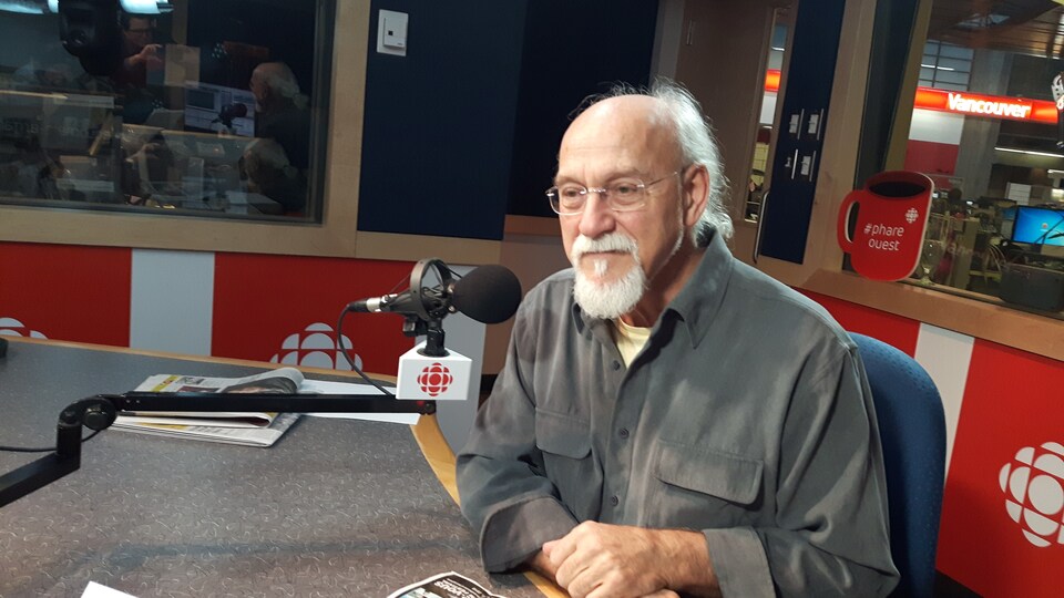 sexagénaire à lunettes assis derrière un micro dans un studio de radio-canada