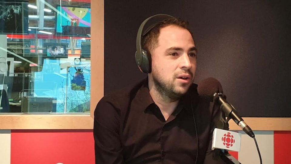 Un homme est assis devant un micro dans une studio de radio.