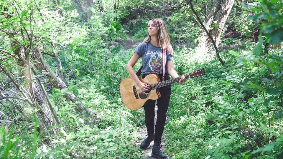 quadragénaire blonde portant guitare en bandoulière dans la forêt