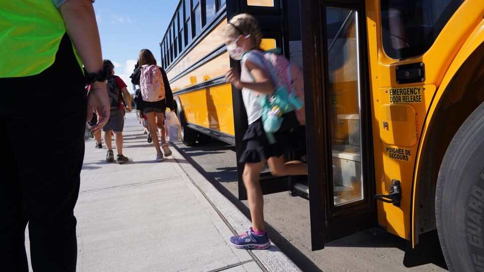 Une petite fille descend de l'autobus scolaire.