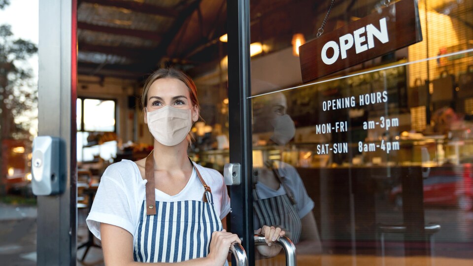 Une femme portant un masque ouvre la porte d'un café.