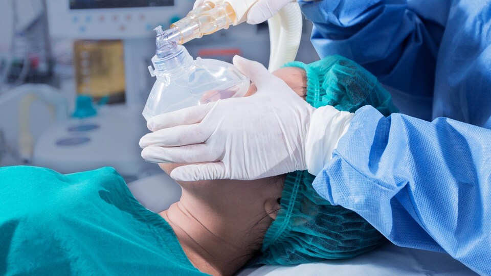 Un employé du réseau de la santé met un masque sur un patient. 
