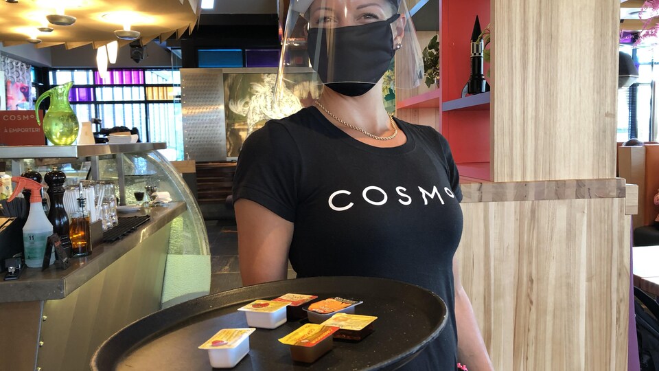 Un serveuse d'un restaurant de Québec qui porte une visière et un masque.