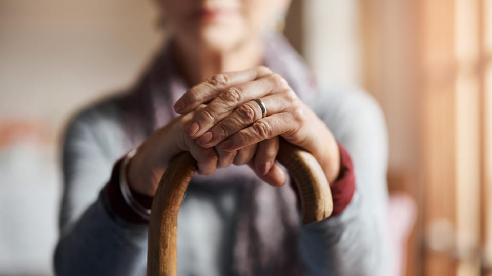 Une personne âgée tient une canne à deux mains.