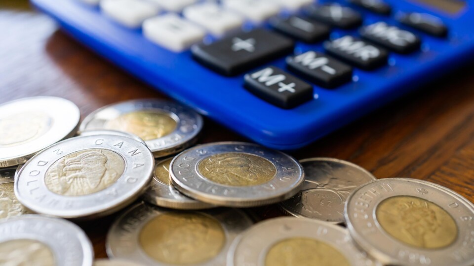 Des pièces de 2 dollars canadiens sur une table, à côté d'une calculatrice.