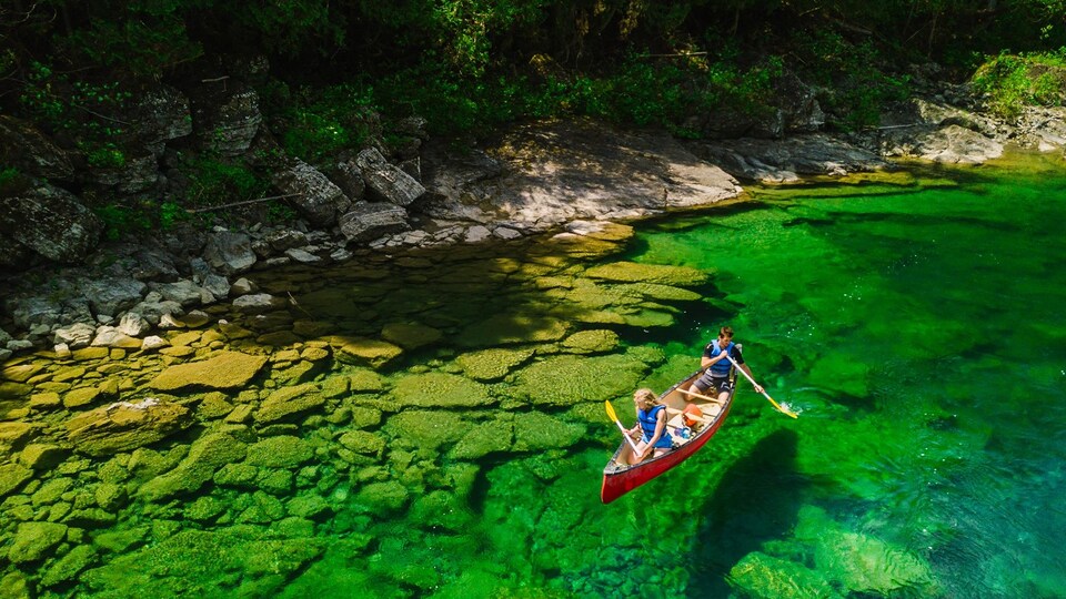 Un canot dévale la rivière photographiée de eaux, ce qui laisse voir des eaux vertes et limpides