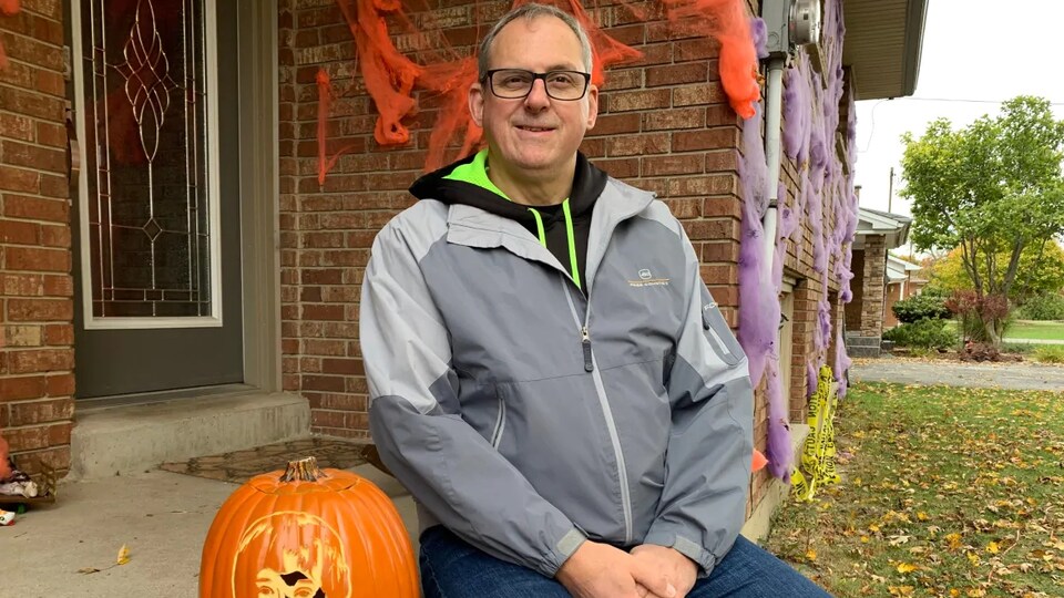 Un homme est assis à côté d'une citrouilles.