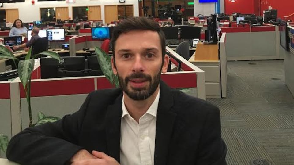 Romain Paulais est appuyé sur une paroie de séparation de bureaux dans une salle de nouvelles.