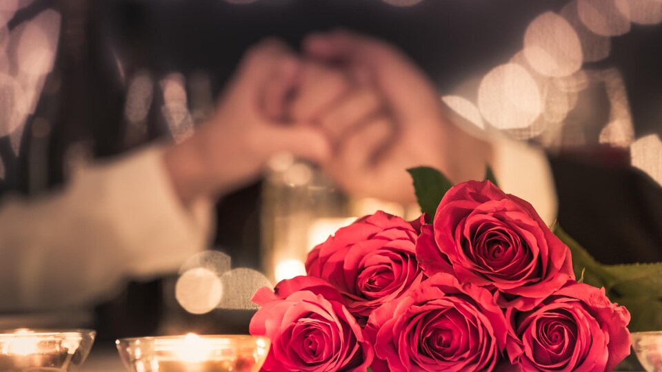 Gros plan sur un bouquet de roses, avec en arrière-plan un couple qui se tient la main.
