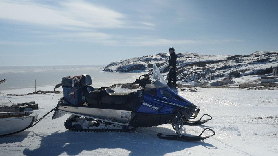 La route Blanche, en Basse-Côte-Nord : on peut voir une motoneige et un homme dans un paysage hivernal, avec vue sur le Saint-Laurent et les montagnes.
