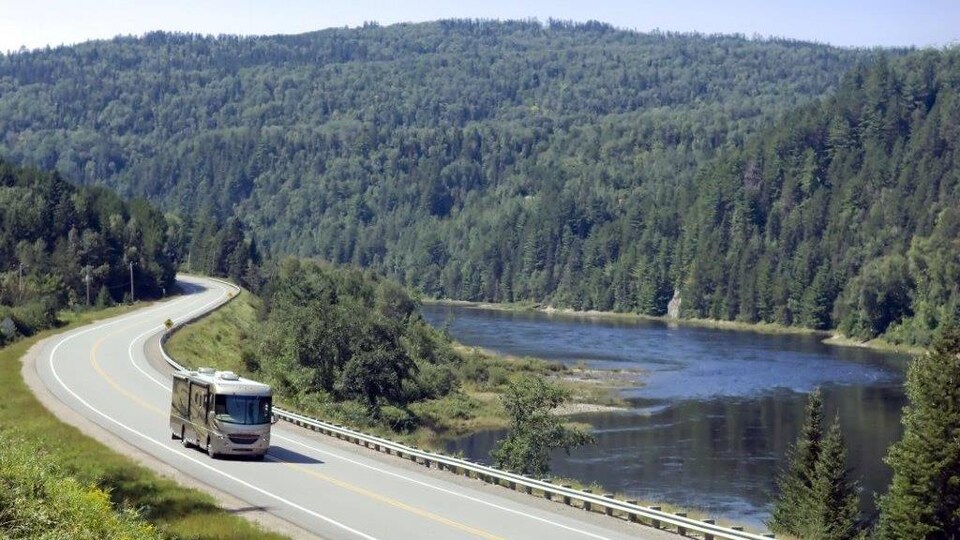Un véhicule récréatif circule sur une route entourée de montagnes et près d'une rivière.