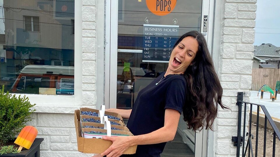 Roxanne tient plusieurs paniers de bleuets locaux devant la porte de son commerce.
