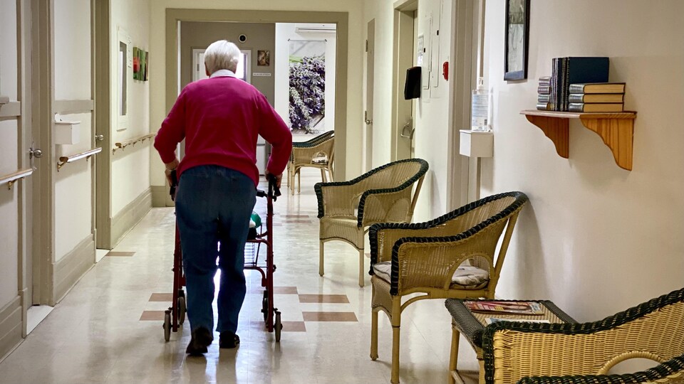 Une personne âgée se déplace en marchette dans le corridor d'une résidence privée pour aînés.