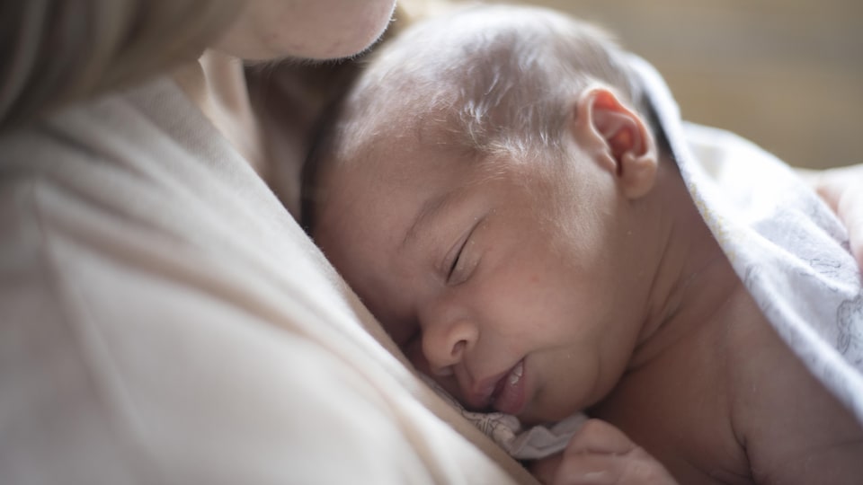 Un nouveau-né dort sur la poitrine de sa mère.  Le bébé est nu et est enveloppé d'une couverture blanche.
