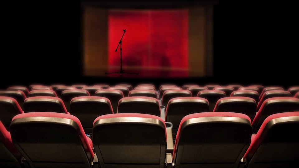 Une salle de spectacle vide avec des sièges rouges et un micro sur une scène également vide.