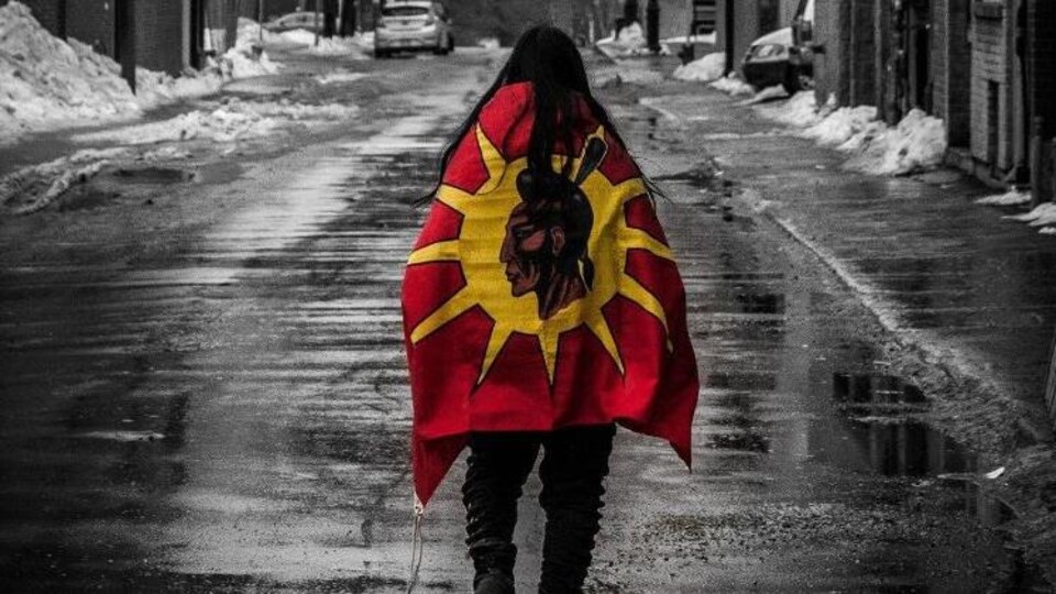 Une personne un drapeau autochtone, marche de dos dans la rue. 