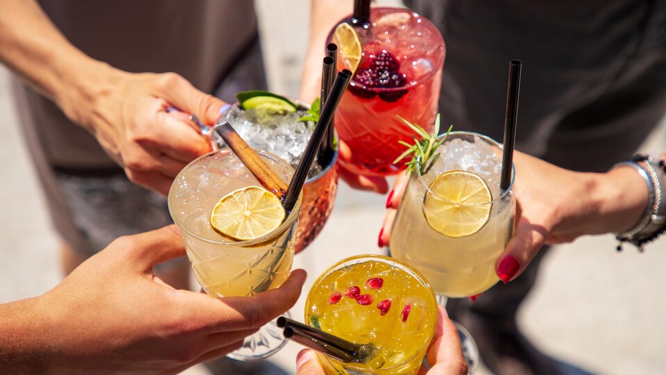 Cinq mains tenant chacune un cocktail pour faire un toast.