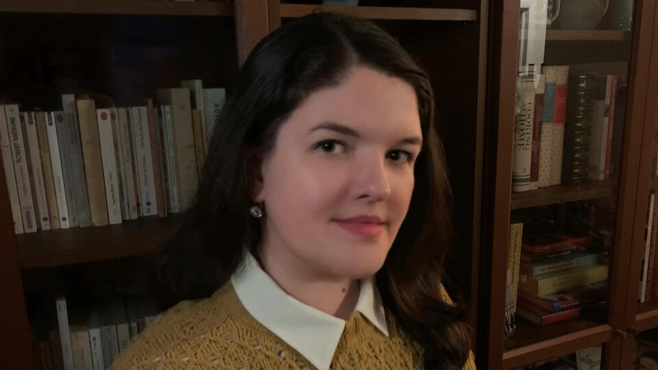 Une jeune femme assise devant une bibliothèque.