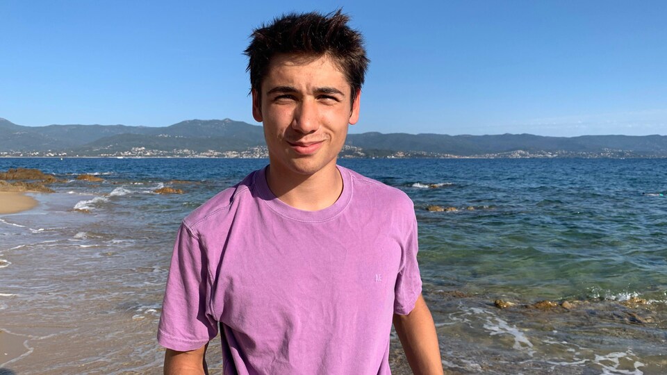 Un jeune homme sur le bord de la baie avec des montagnes en fond.