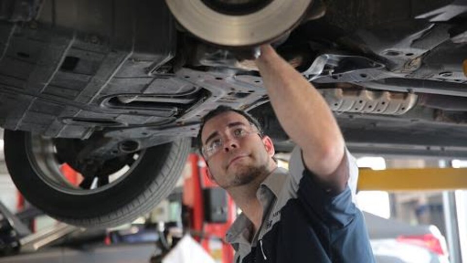 Un homme inspecte le châssis d'une voiture.