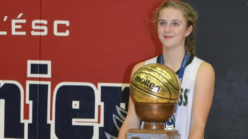 Une jeune joueuse de basketball qui tient un trophée dans ses mains.