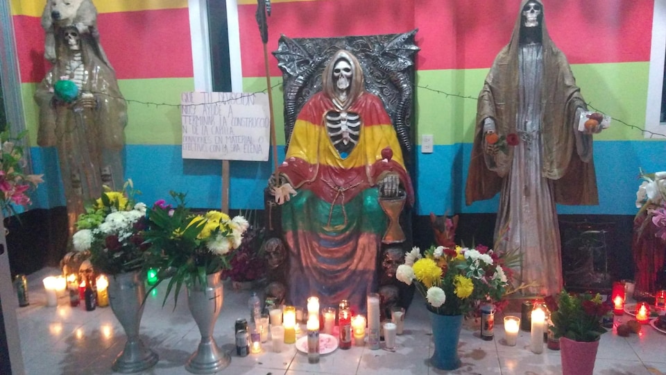 Des bougies et des fleurs déposées devant trois statues de squelettes