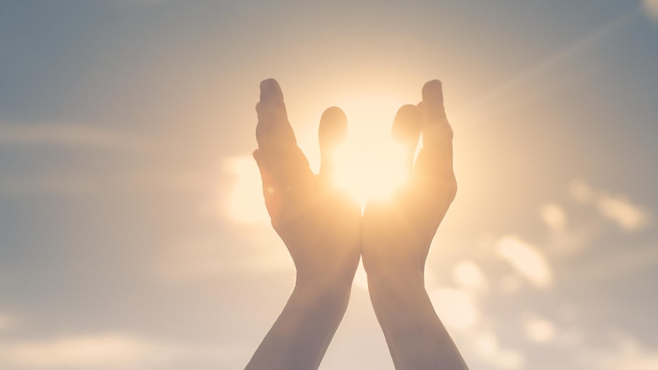 Une personne tient ses mains en l'air comme pour attraper le soleil.
