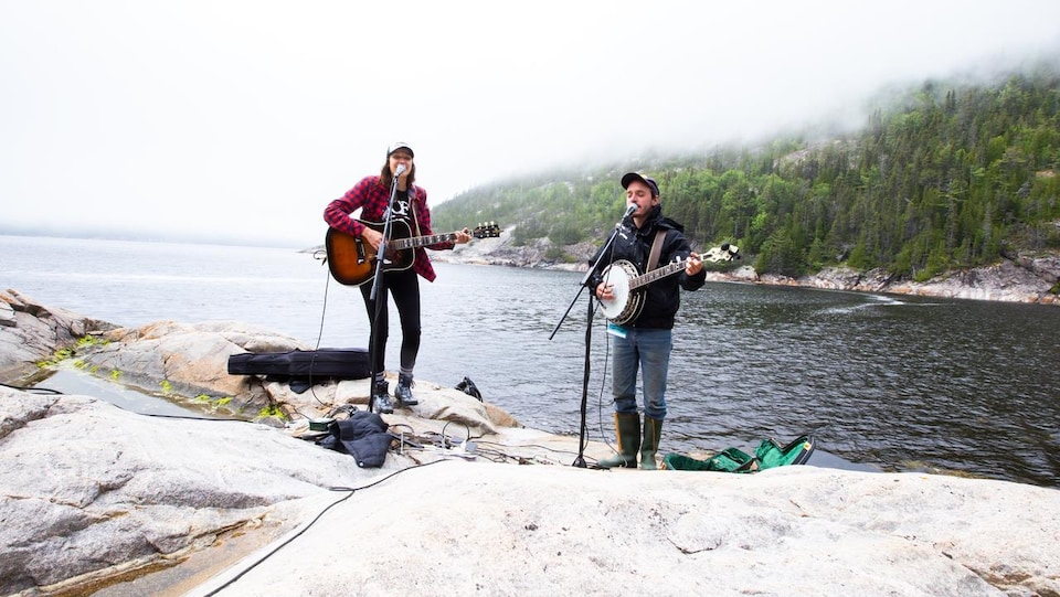 Deux musiciens sur des roches près de l'eau.