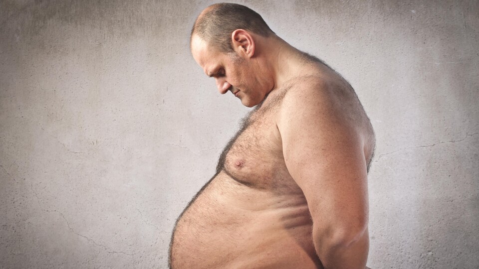 Un homme triste observe son ventre. 