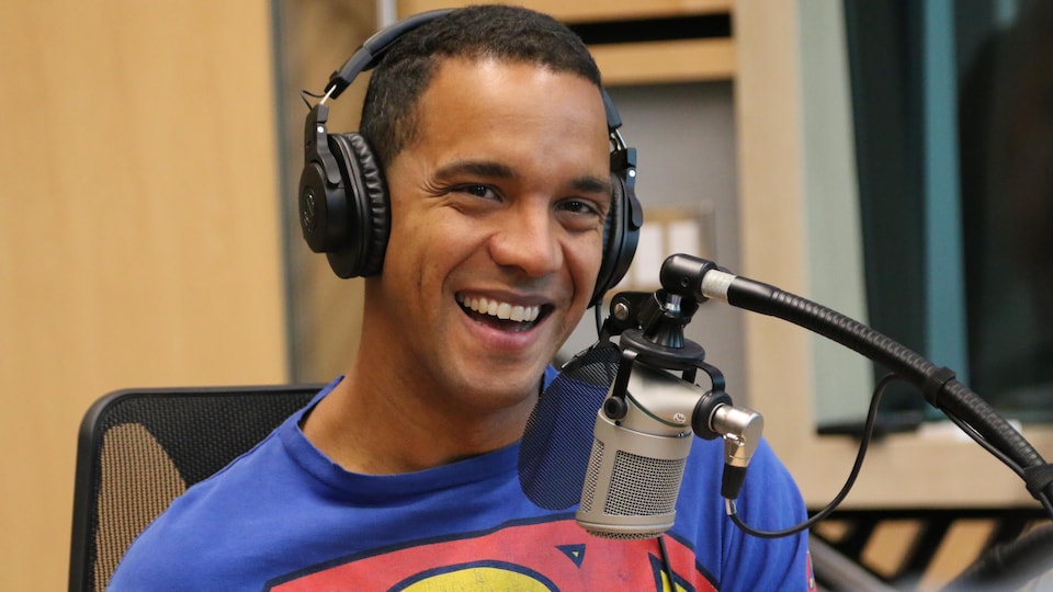 Un homme, casque d'écoute sur la tête, a un large sourire lors d'une entrevue dans un studio de radio. 