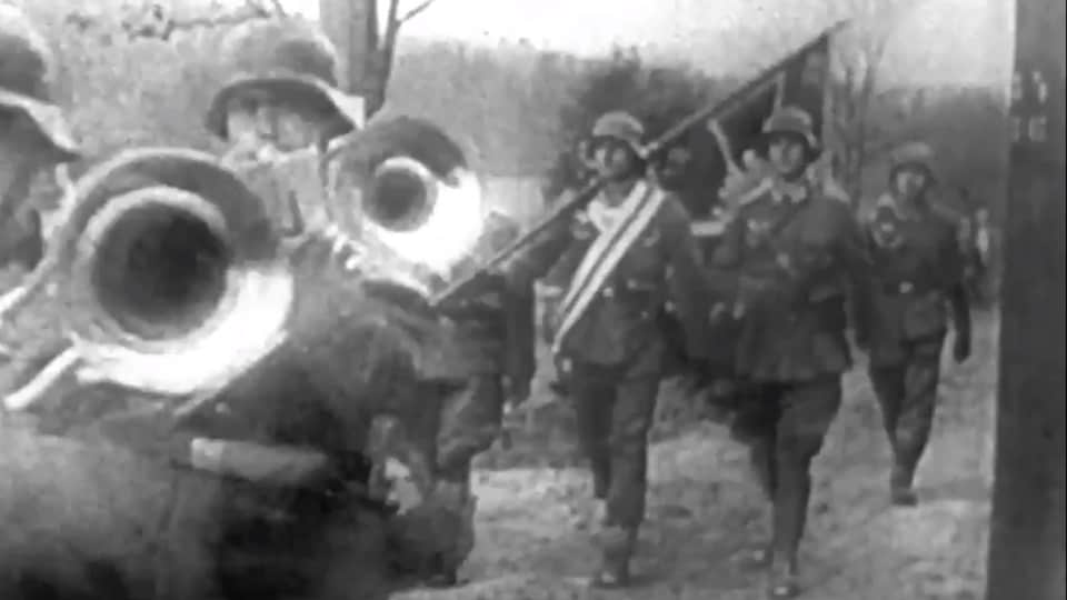 Des soldats allemands avec trompettes et drapeaux avancent sur un chemin vers la Pologne. 
