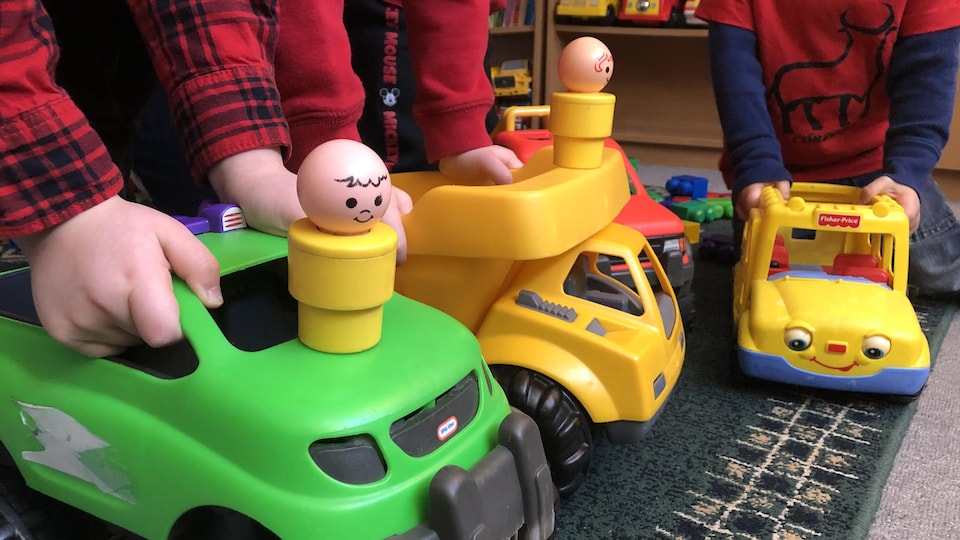 Trois enfants non-identifiés d'âge préscolaire jouent ensemble avec des camions-jouets dans un service de garde.