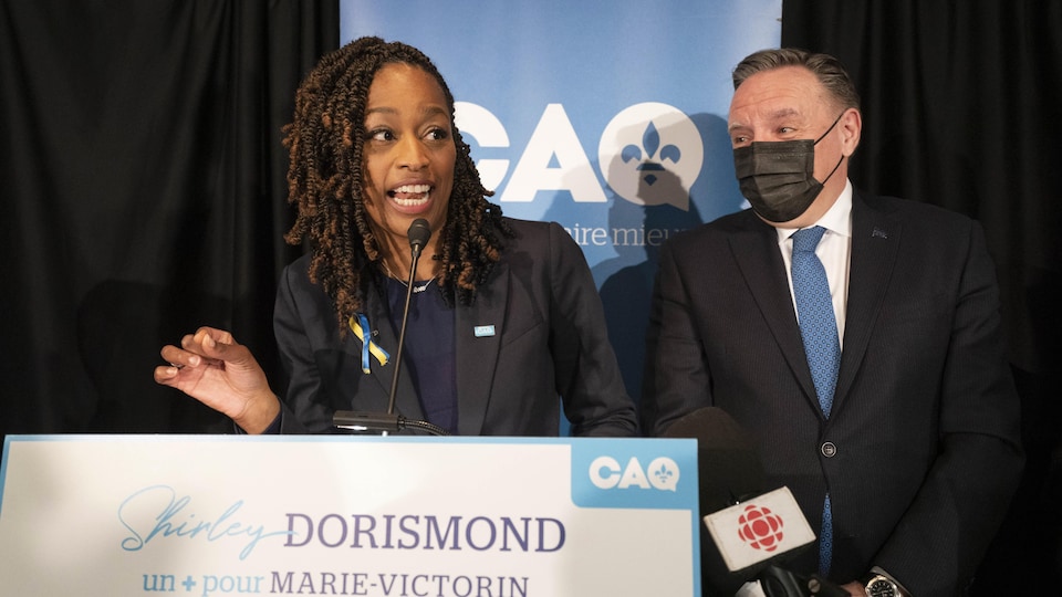 Si Ms.  Dorismond talks to CAQ activists.  François Legault, wearing a mask, listens to him.