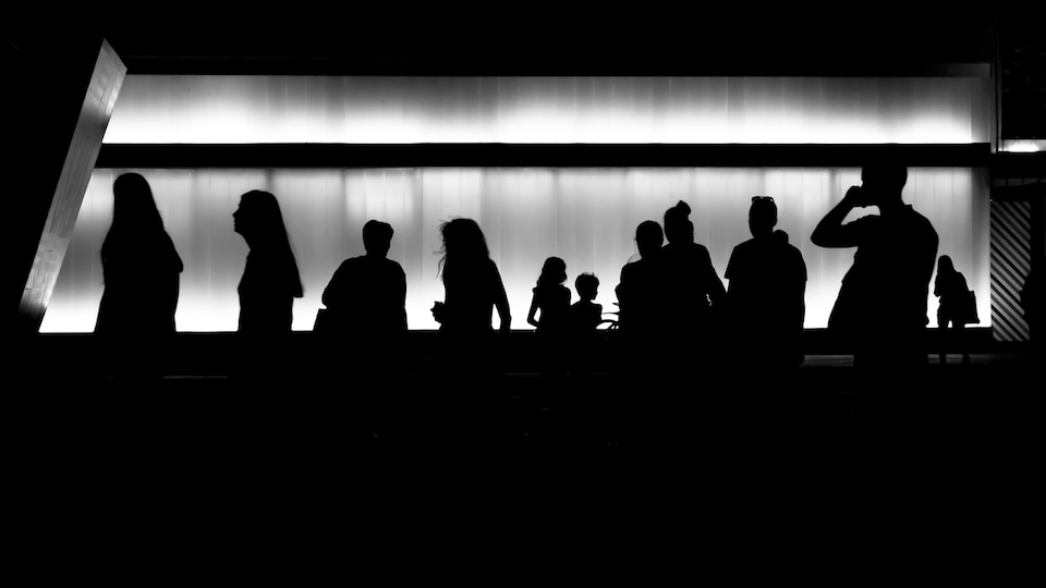 Une douzaine de silhouettes humaines sur un fond métallique illuminé