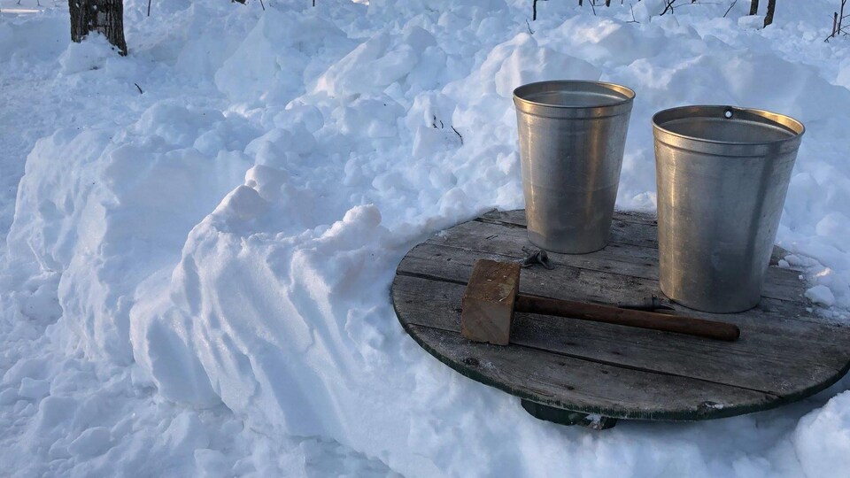 Deux chaudières pour l’eau d’érable et un maillet de bois déposés sur une table dans l’érablière