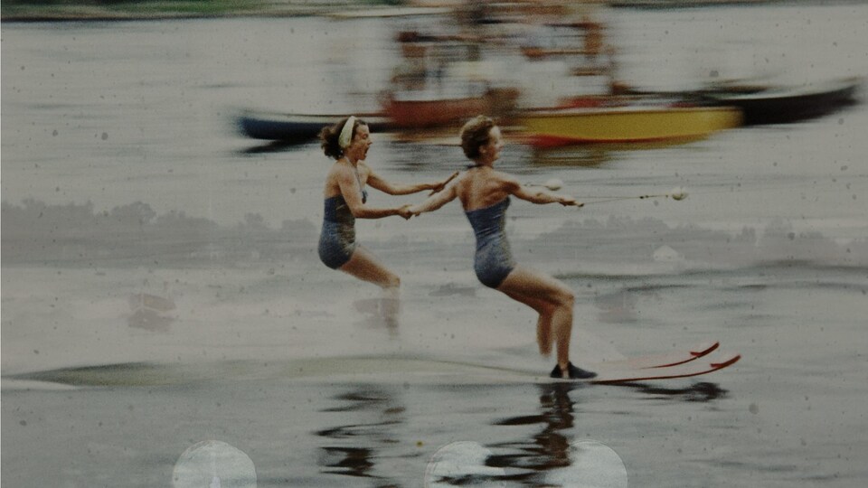 Deux femmes font du ski nautique en se tenant la main sur la rivière des Mille-Îles. Photogramme 16mm altéré transféré en numérique tiré du film documentaire "Au pays des Mille-Îles" de Lisa Sfriso.